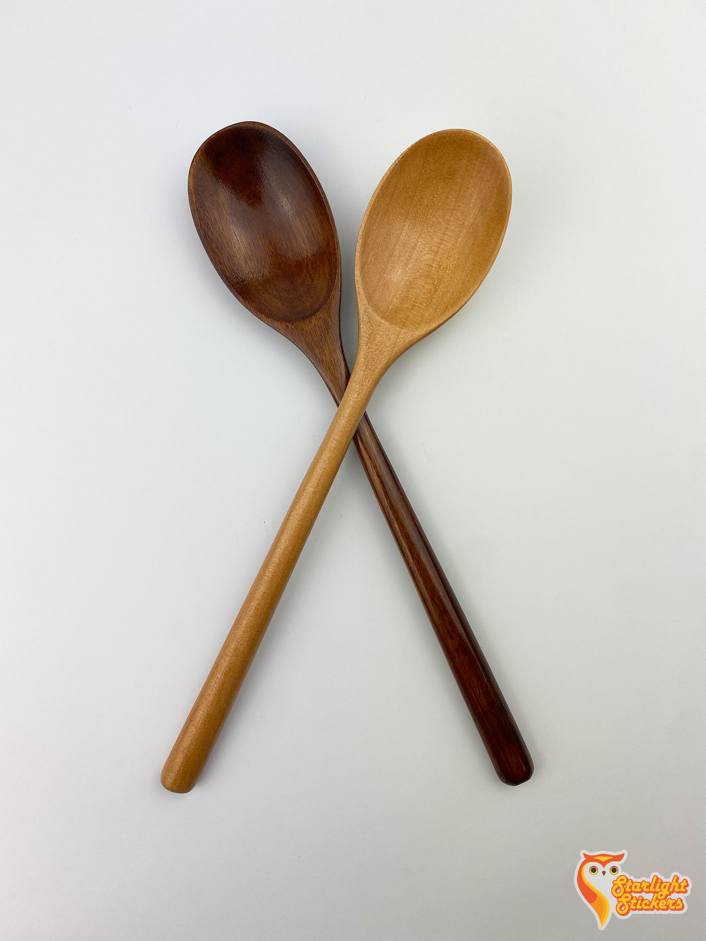Dark wood and light wood spoon making an "X" on a white background.