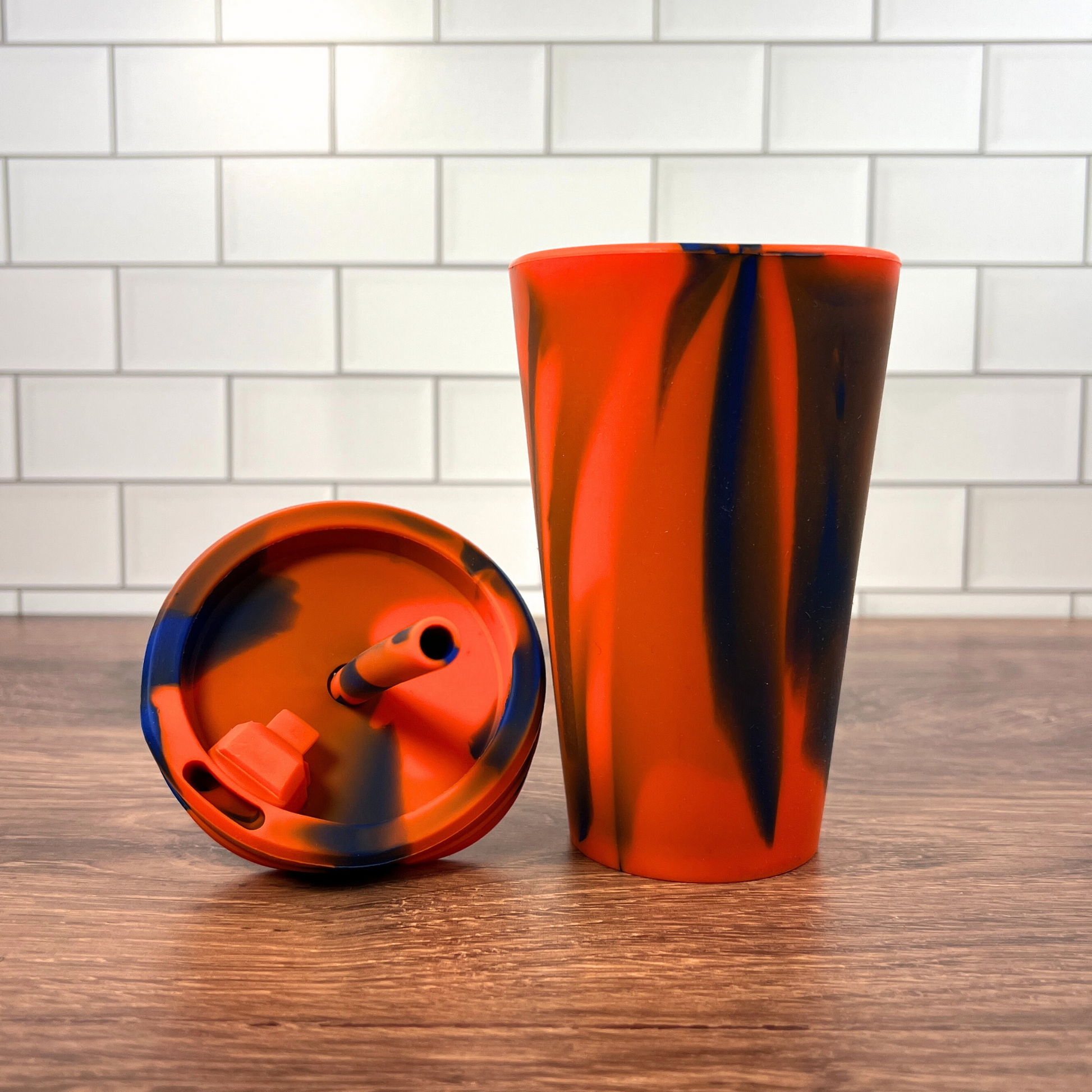 Orange and blue silicone cup on a wooden table with the lid resting next to it.